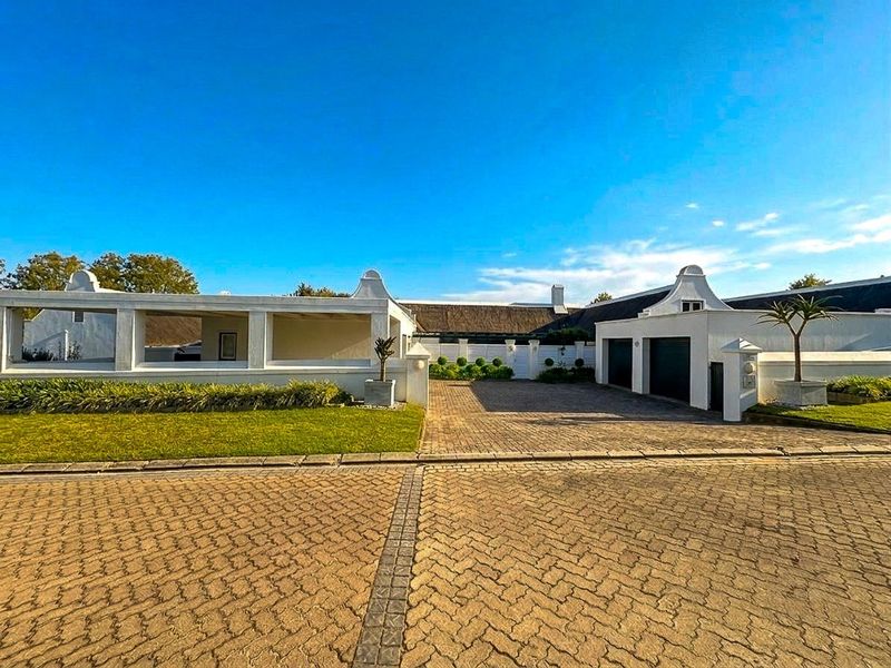 Front view of a well-maintained property featuring a paved driveway, double garage, and distinctive gabled architecture with a thatched roof.