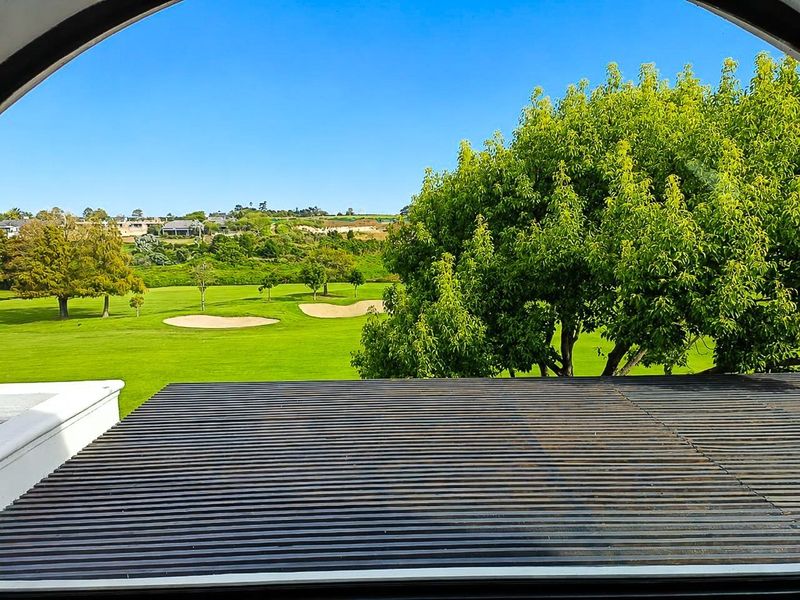 A scenic elevated view overlooking a lush green golf course with sand bunkers, framed by a slatted roof structure.