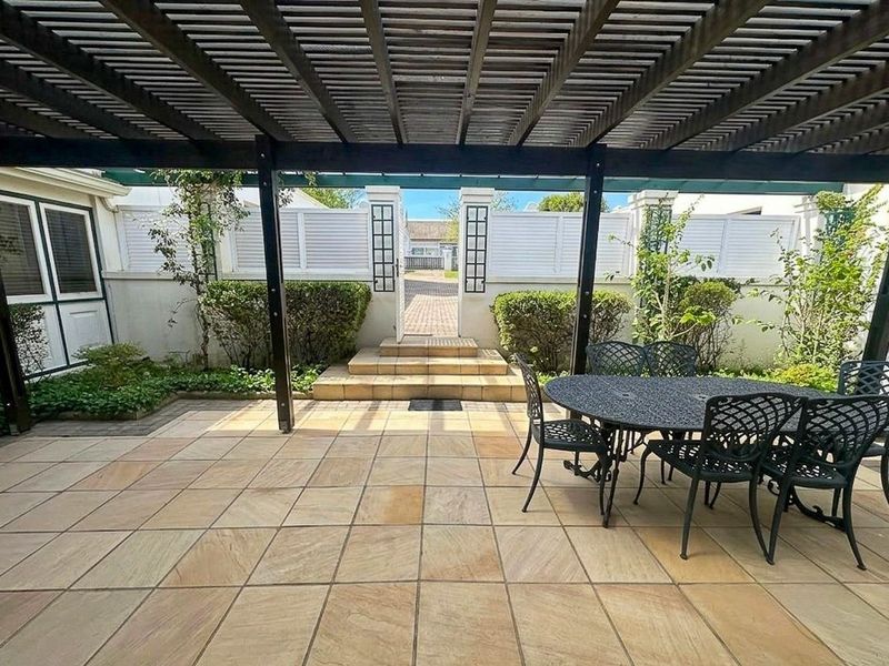 A well-maintained covered patio featuring a timber pergola and sandstone paving, providing a seamless transition to the rear garden area.