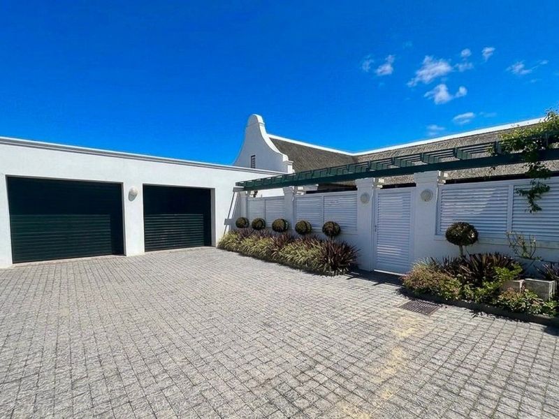 Front exterior view featuring a paved driveway, double garage, pedestrian gate, and a pergola, showcasing a well-maintained property with a classic thatched roof.