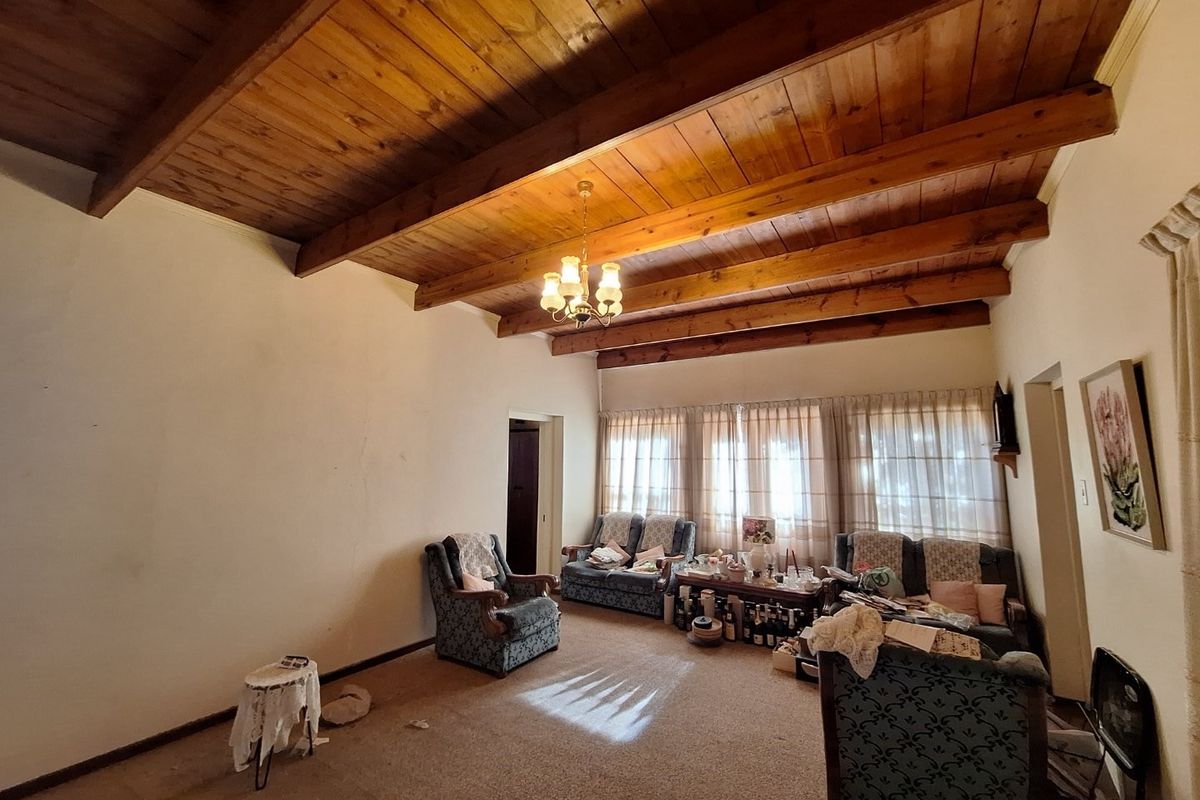 A spacious living room featuring exposed timber beam ceilings and large windows, offering a classic aesthetic with potential for modern updates.