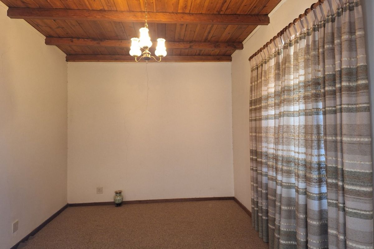 A vacant bedroom featuring a rustic exposed timber beam ceiling, carpeted flooring, and a large window with fitted curtains.