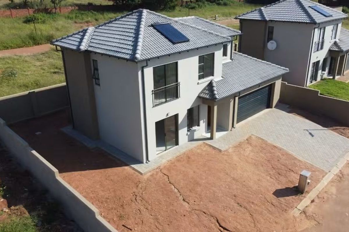 Aerial view of a modern two-story residential house featuring a tiled roof, solar water heating system, paved driveway, and perimeter boundary walls.