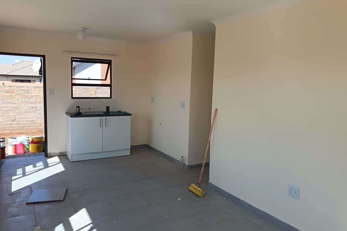 A compact, empty kitchen area featuring basic built-in cabinetry, a sink, and tiled flooring, providing a clean slate for customization.