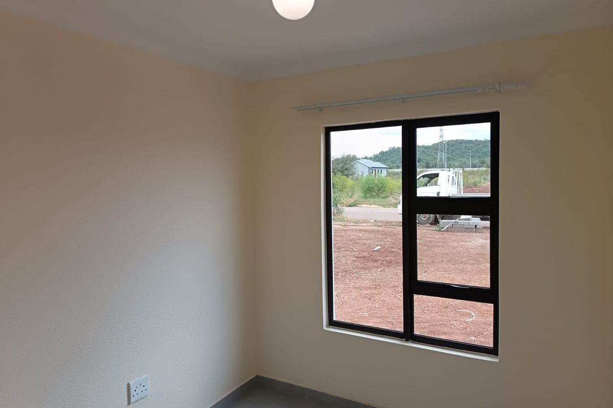 A clean, empty bedroom featuring neutral walls, tiled flooring, and a modern black aluminium window frame with a curtain rod installed.