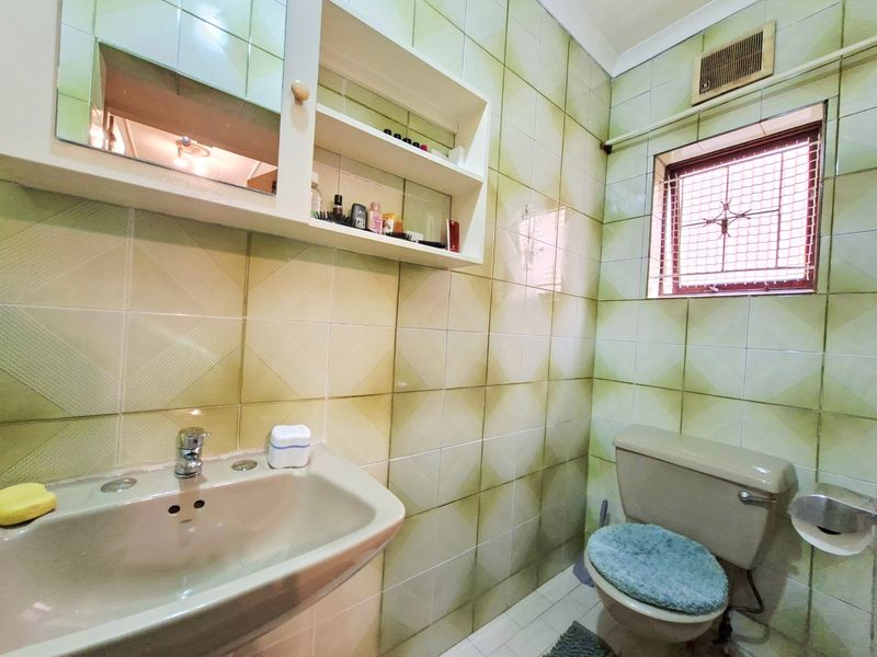 A compact bathroom featuring dated wall tiles, a wall-mounted basin, a toilet, and a built-in medicine cabinet with shelving.