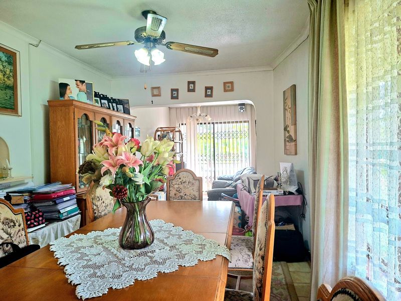 A dining area featuring a ceiling fan and an open-plan layout leading into an adjacent living space with sliding door access to the outdoors.