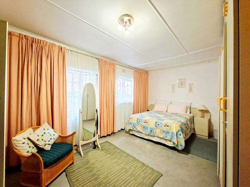 A spacious bedroom featuring large windows with floor-to-ceiling curtains, built-in cupboards, and a central ceiling light fixture.