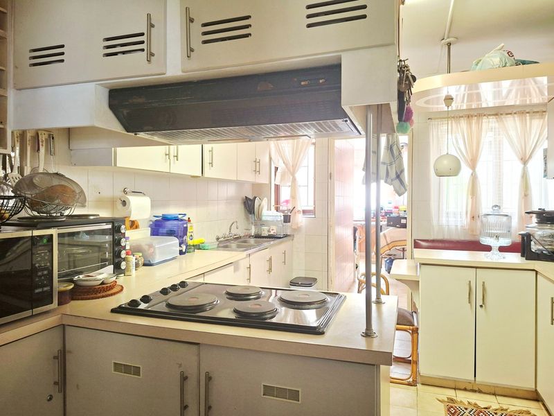 A dated kitchen featuring original cabinetry, a built-in electric hob, and an integrated extractor fan, offering a functional layout with potential for modernization.