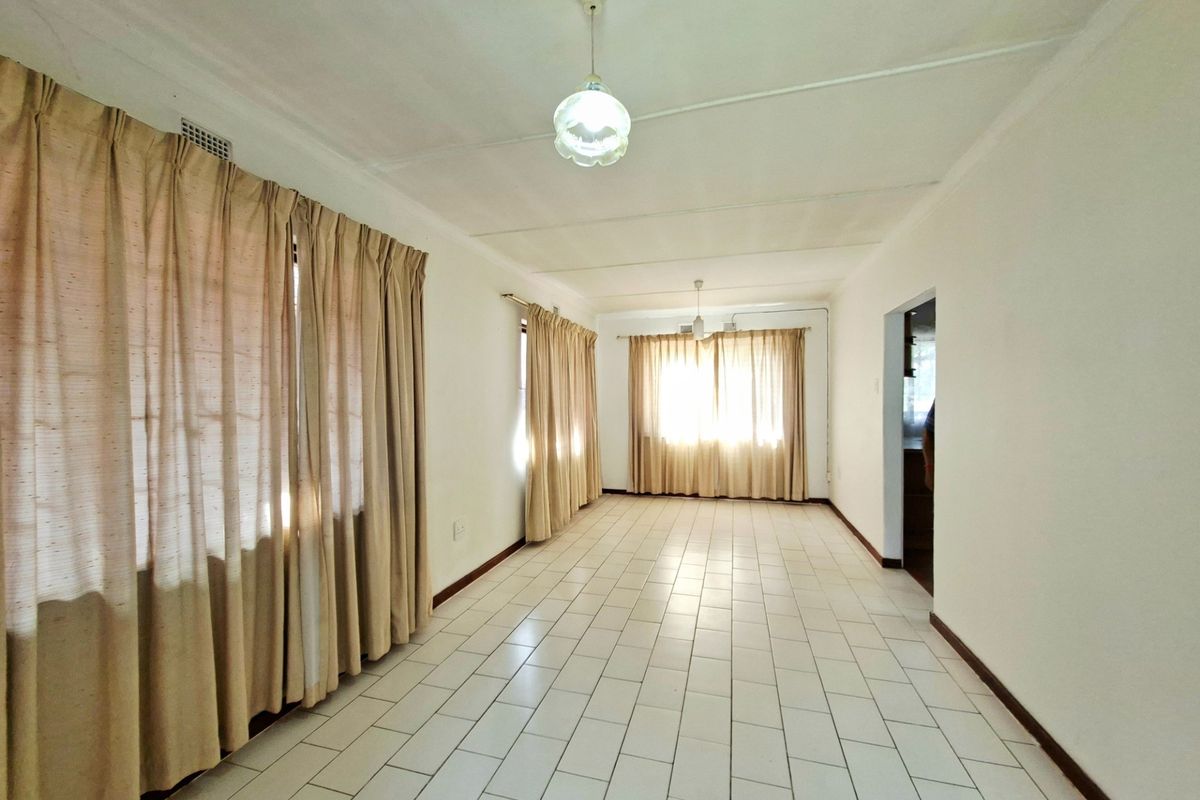 A spacious, empty living area featuring white tiled flooring, neutral walls, and multiple windows with curtains, offering a blank canvas for interior design.