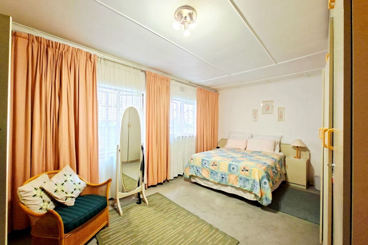 A spacious bedroom featuring large windows with floor-to-ceiling curtains, built-in cupboards, and a central ceiling light fixture.