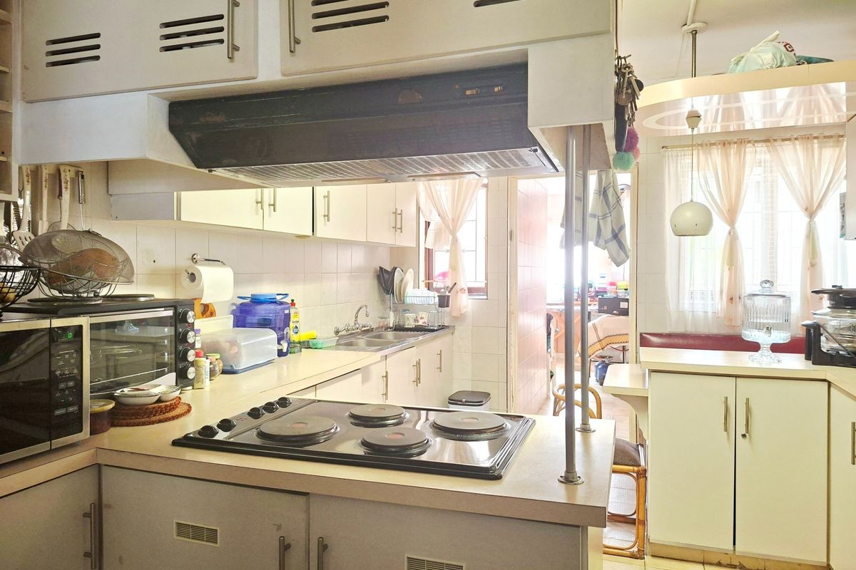 A dated kitchen featuring original cabinetry, a built-in electric hob, and an integrated extractor fan, offering a functional layout with potential for modernization.