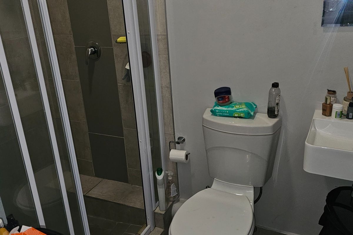 Compact bathroom featuring a glass-enclosed shower, wall-mounted basin, and standard toilet, finished with neutral wall tiles and flooring.