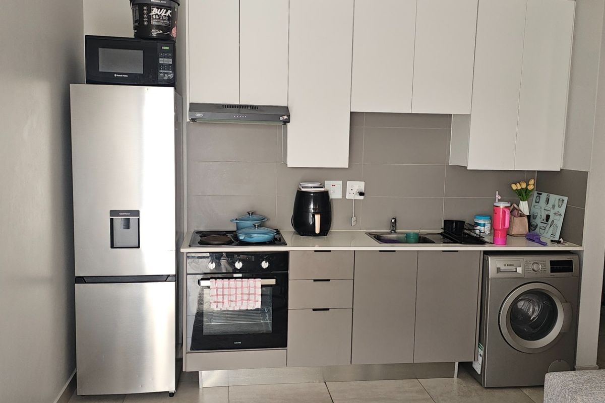 Modern compact kitchen featuring white upper cabinetry, grey lower cabinets, integrated oven, hob, extractor fan, and space for a washing machine.
