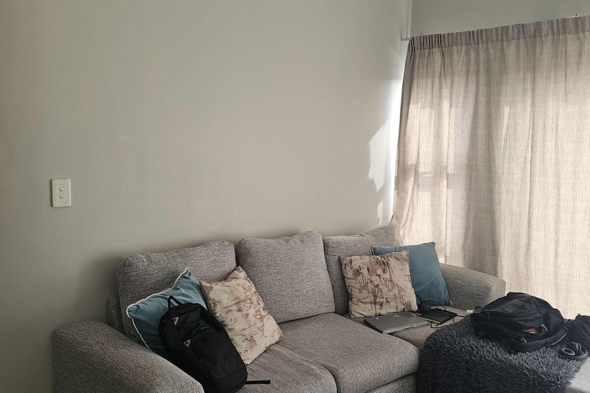 A living room area featuring neutral wall tones and a large window covered by floor-to-ceiling curtains, providing natural light to the space.