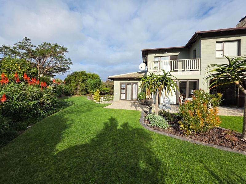 A well-maintained rear garden featuring a paved patio area, lush lawn, and established landscaping, adjacent to the two-story residential building.