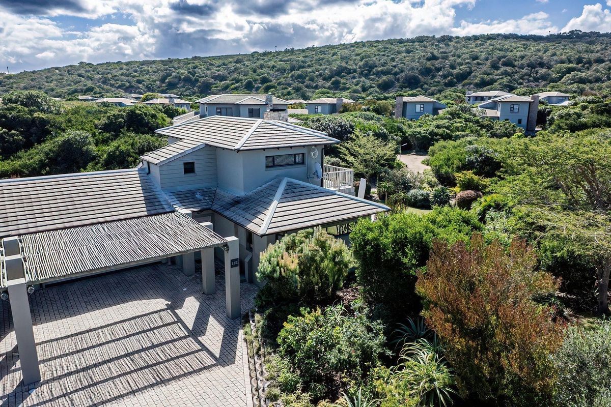 Aerial view of a modern residential property featuring a tiled roof, paved driveway, and a covered carport, set within a lush, landscaped estate environment.