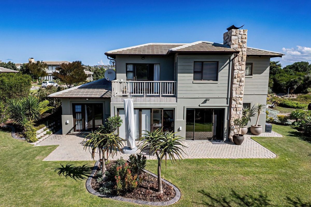 A well-maintained two-story residence featuring a stone-clad chimney, paved patio area, upper-level balcony, and landscaped garden surroundings.