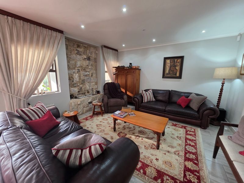 A comfortable living room featuring a prominent natural stone fireplace feature wall, recessed downlighting, and tiled flooring.