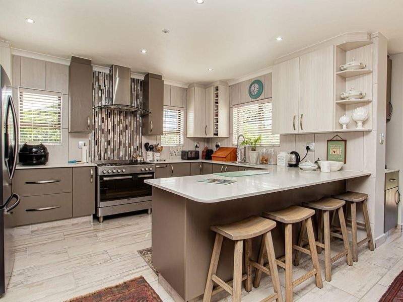 Modern kitchen featuring a central island with breakfast bar, stone countertops, stainless steel gas stove, extractor fan, and ample cabinetry.
