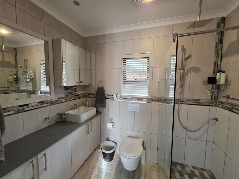 Modern bathroom featuring a glass-enclosed walk-in shower, wall-mounted toilet, and a vanity with a vessel sink and mirrored cabinetry.