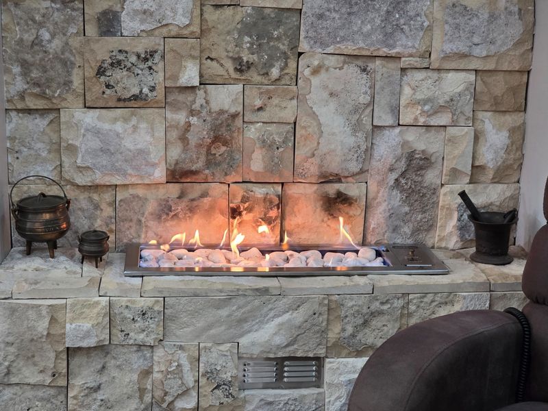 A modern built-in gas fireplace featuring a decorative stone-clad surround and a sleek stainless steel burner tray with white fire stones.