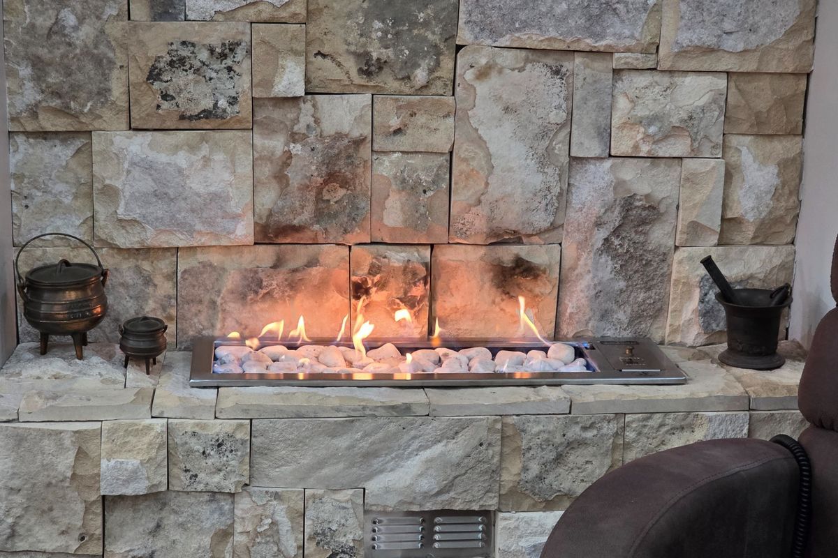 A modern built-in gas fireplace featuring a decorative stone-clad surround and a sleek stainless steel burner tray with white fire stones.