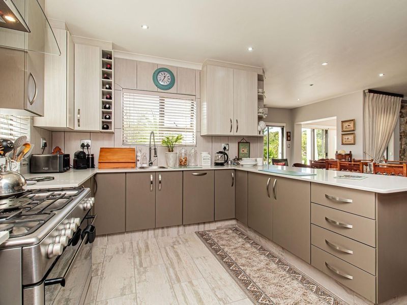 Modern open-plan kitchen featuring two-tone cabinetry, stone countertops, stainless steel gas range, and integrated lighting, flowing into the adjacent dining area.