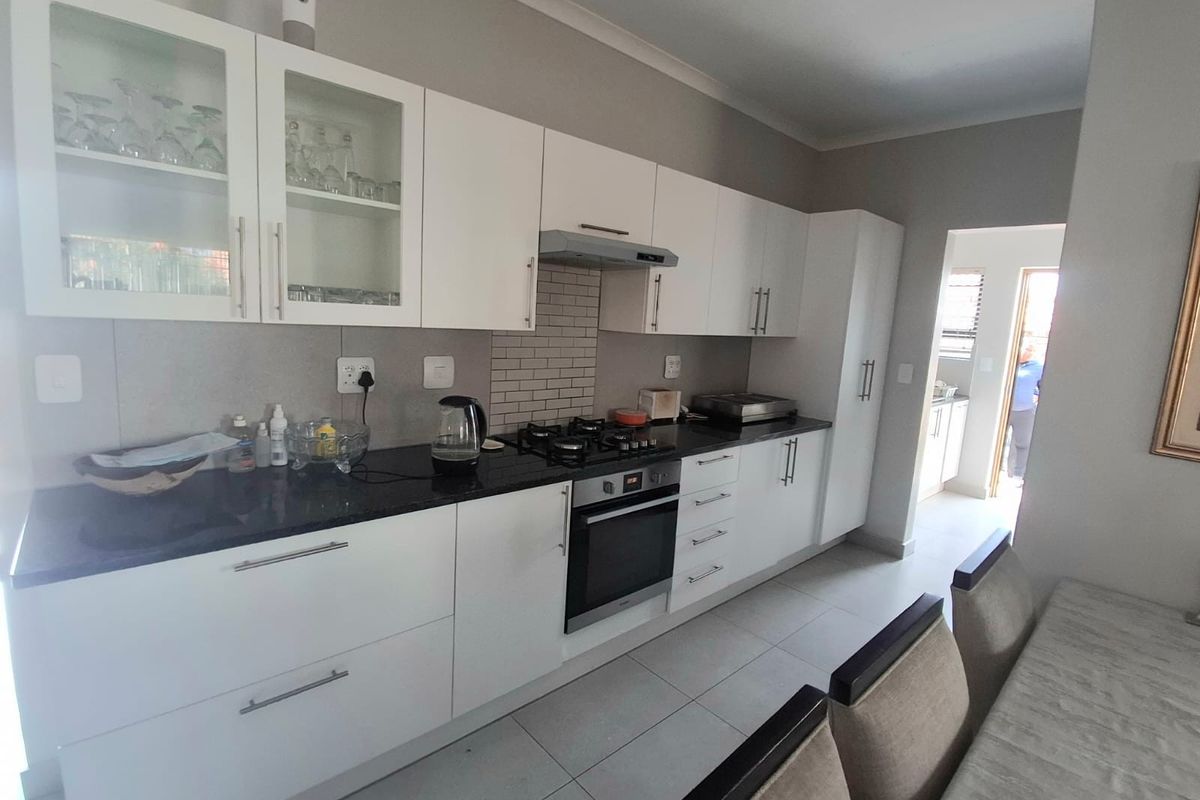 Modern kitchen featuring white cabinetry, dark granite countertops, built-in oven, gas hob, and a tiled backsplash, leading into a secondary utility area.