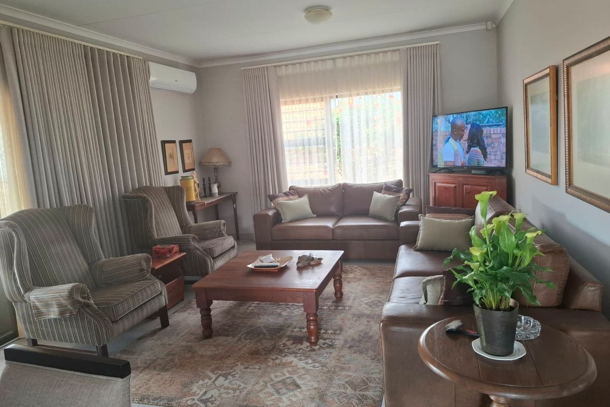 A comfortable living room featuring tiled flooring, large windows with floor-to-ceiling curtains, and a wall-mounted air conditioning unit.