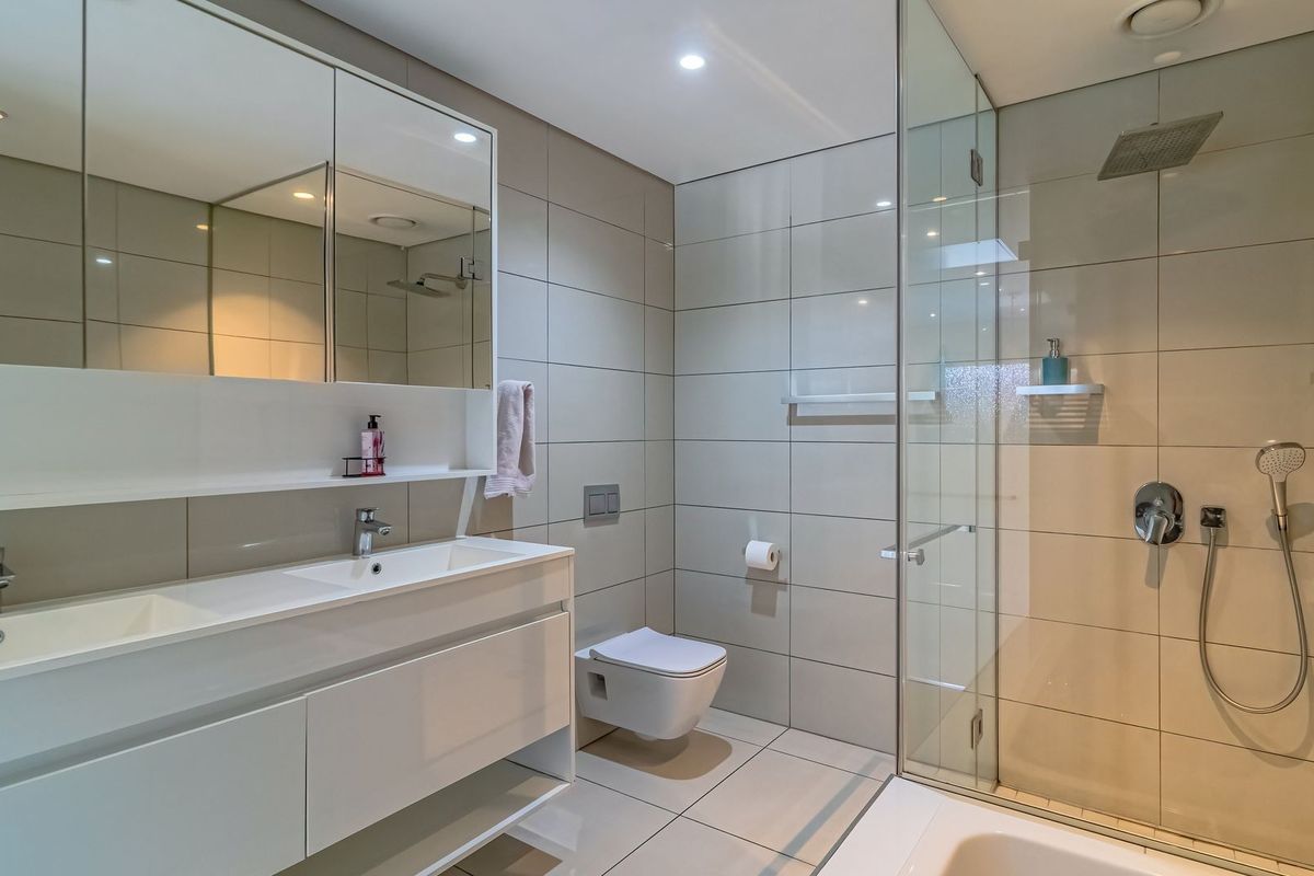 Modern bathroom featuring a double vanity with integrated mirrors, a wall-mounted toilet, and a spacious walk-in glass shower with a rainfall showerhead.