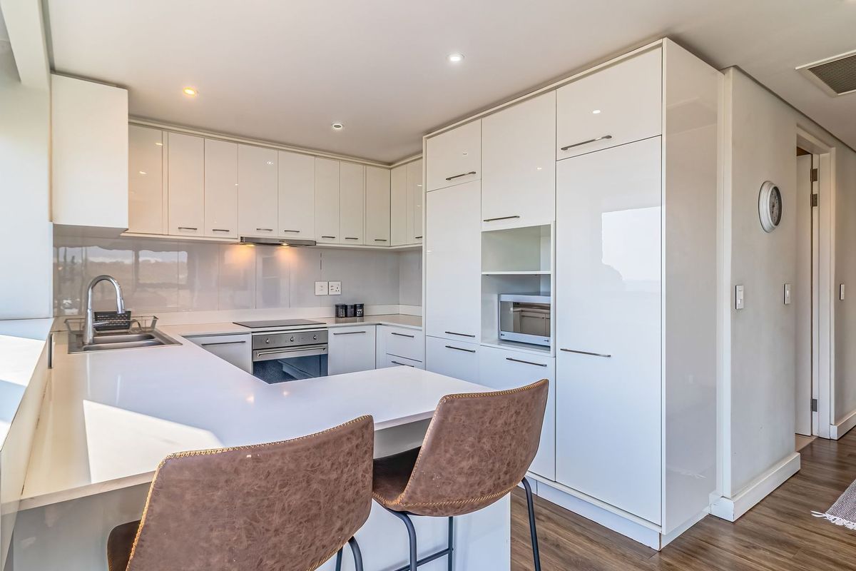 Modern kitchen featuring high-gloss white cabinetry, integrated appliances, sleek countertops, and a breakfast bar, offering a clean and contemporary aesthetic.