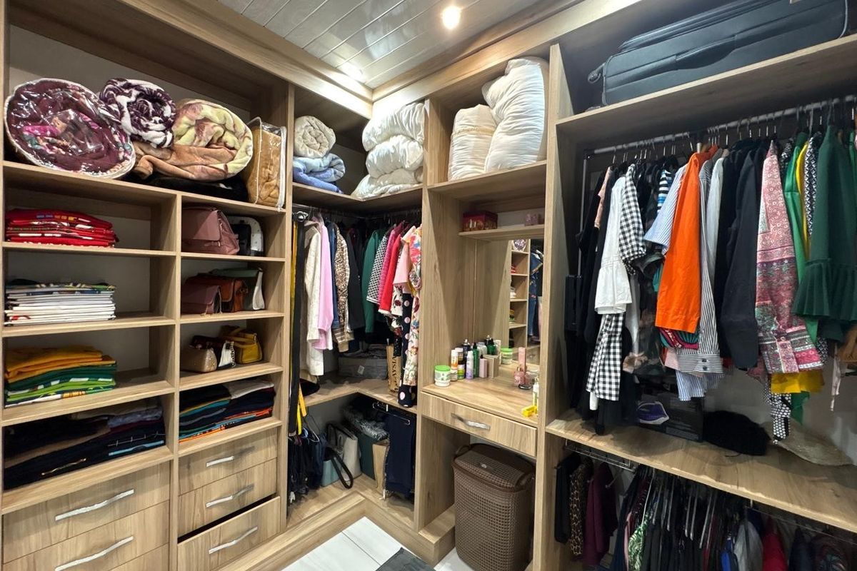 A well-organized walk-in closet featuring extensive built-in wooden cabinetry, shelving, hanging rails, and a dedicated vanity area with integrated mirror.