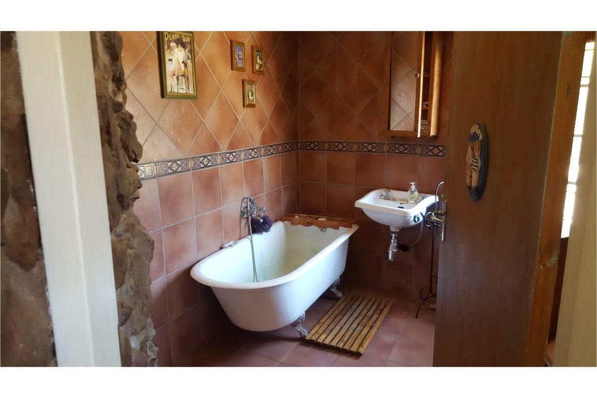A rustic-style bathroom featuring a classic clawfoot bathtub, wall-mounted basin, and warm-toned ceramic tiling with decorative accents.