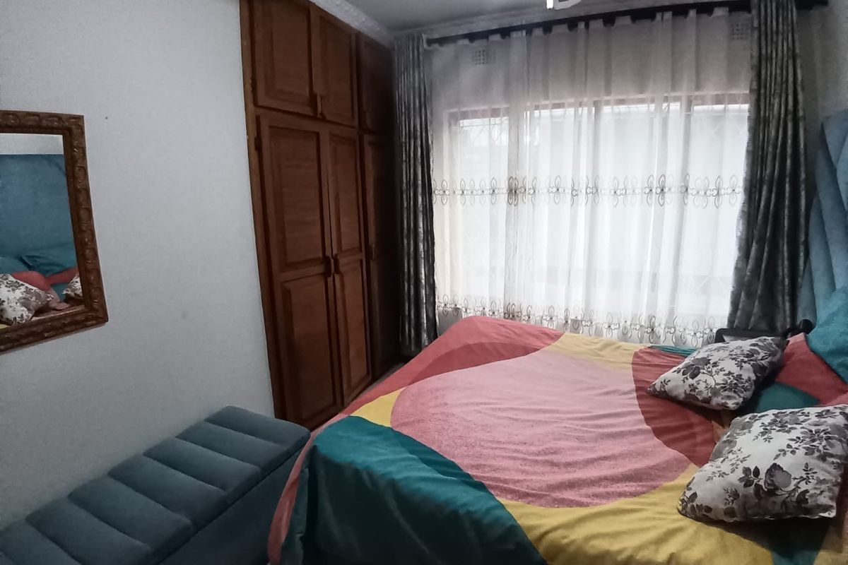A bedroom featuring built-in wooden cupboards, decorative ceiling cornices, and a large window with curtains.