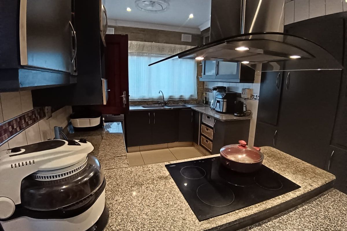 A functional kitchen featuring granite countertops, dark cabinetry, a built-in electric hob, and a modern stainless steel extractor fan.