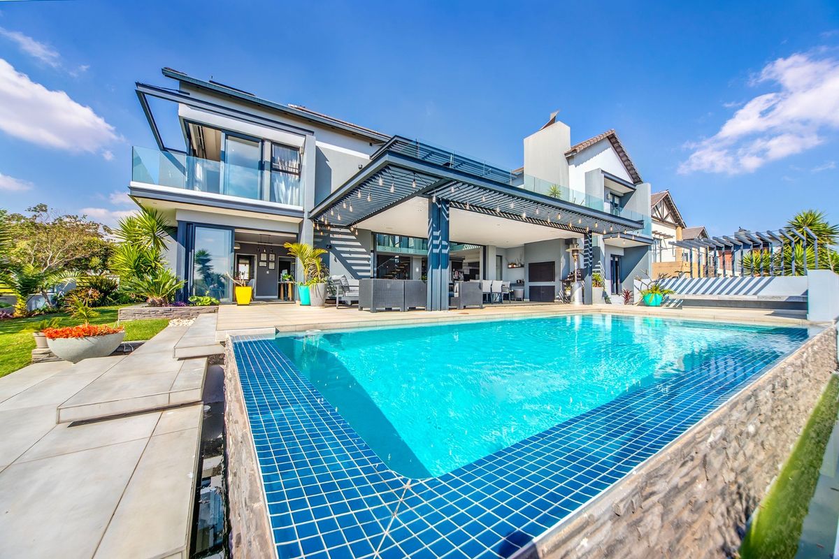 Modern rear exterior featuring a sparkling swimming pool, expansive tiled patio, covered pergola, and contemporary architectural design with glass balcony railings.