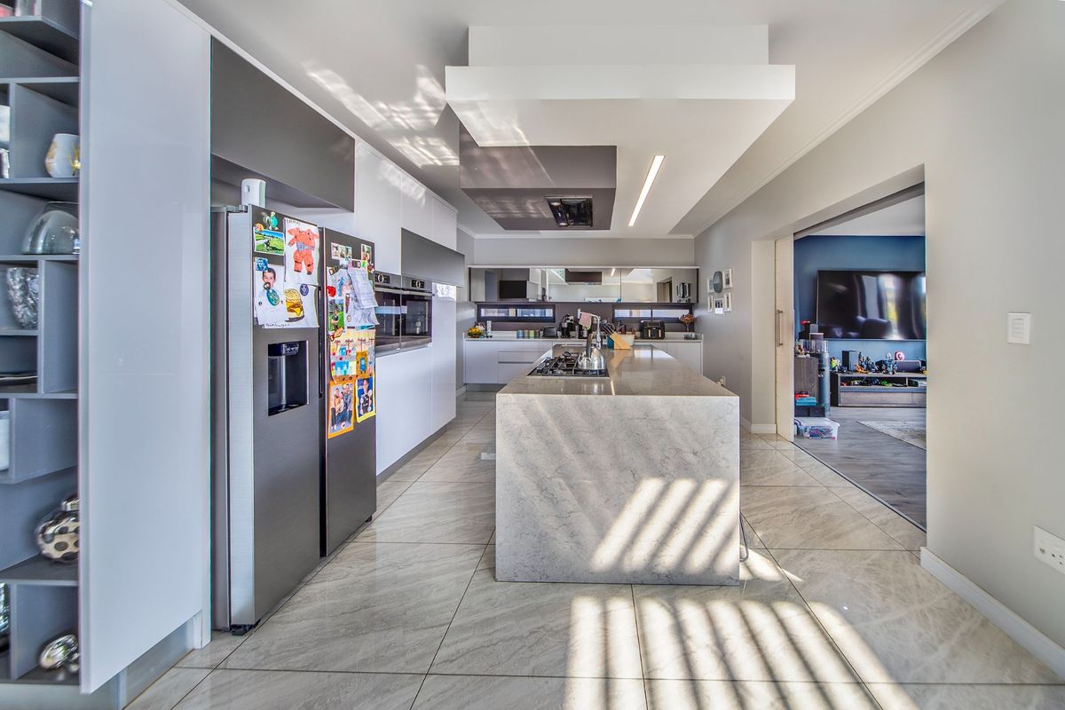 Modern kitchen featuring a large stone-topped island, built-in ovens, sleek cabinetry, and tiled flooring, seamlessly flowing into the adjacent living area.