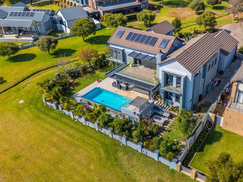 Aerial view of a modern two-story residence featuring a swimming pool, landscaped garden, covered patio, and rooftop solar panels.