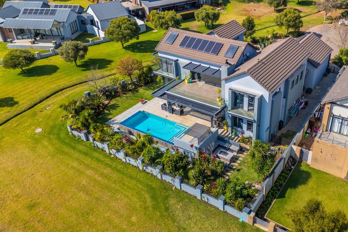 Aerial view of a modern two-story residence featuring a swimming pool, landscaped garden, covered patio, and rooftop solar panels.