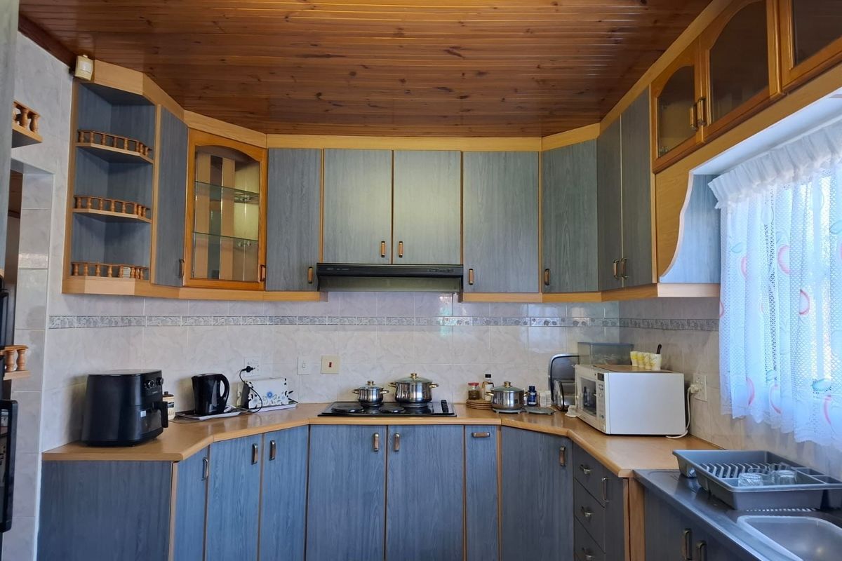 A functional kitchen featuring blue-toned cabinetry, laminate countertops, a built-in hob with extractor fan, and a timber-paneled ceiling.