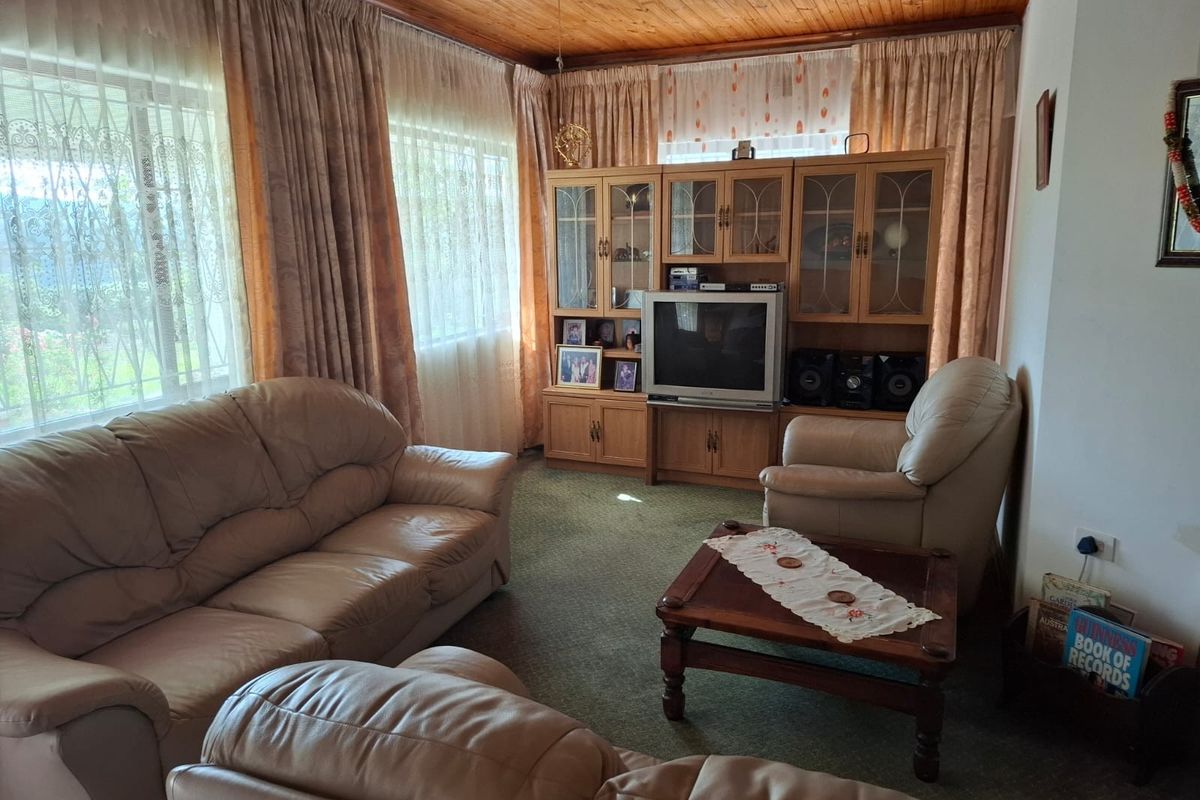 A traditional living room featuring a timber-paneled ceiling, carpeted flooring, and large windows with curtains, offering a comfortable and classic living space.