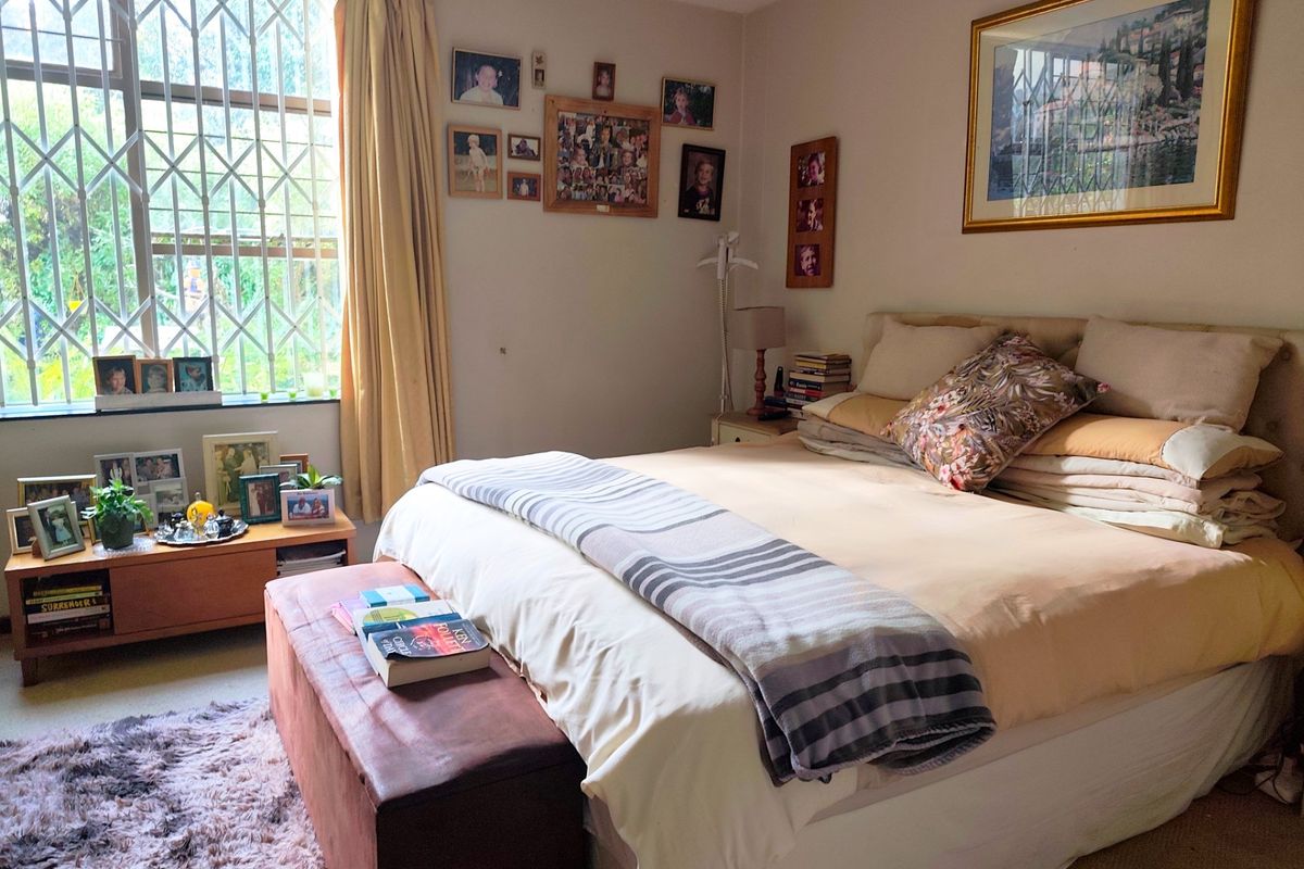 A comfortable bedroom featuring a large window with security bars, neutral carpeting, and ample space for a double bed.