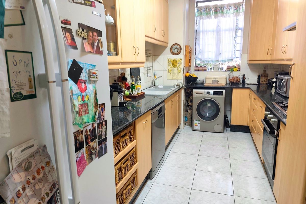 A functional galley-style kitchen featuring light wood cabinetry, dark granite countertops, integrated oven, and built-in laundry appliance space.