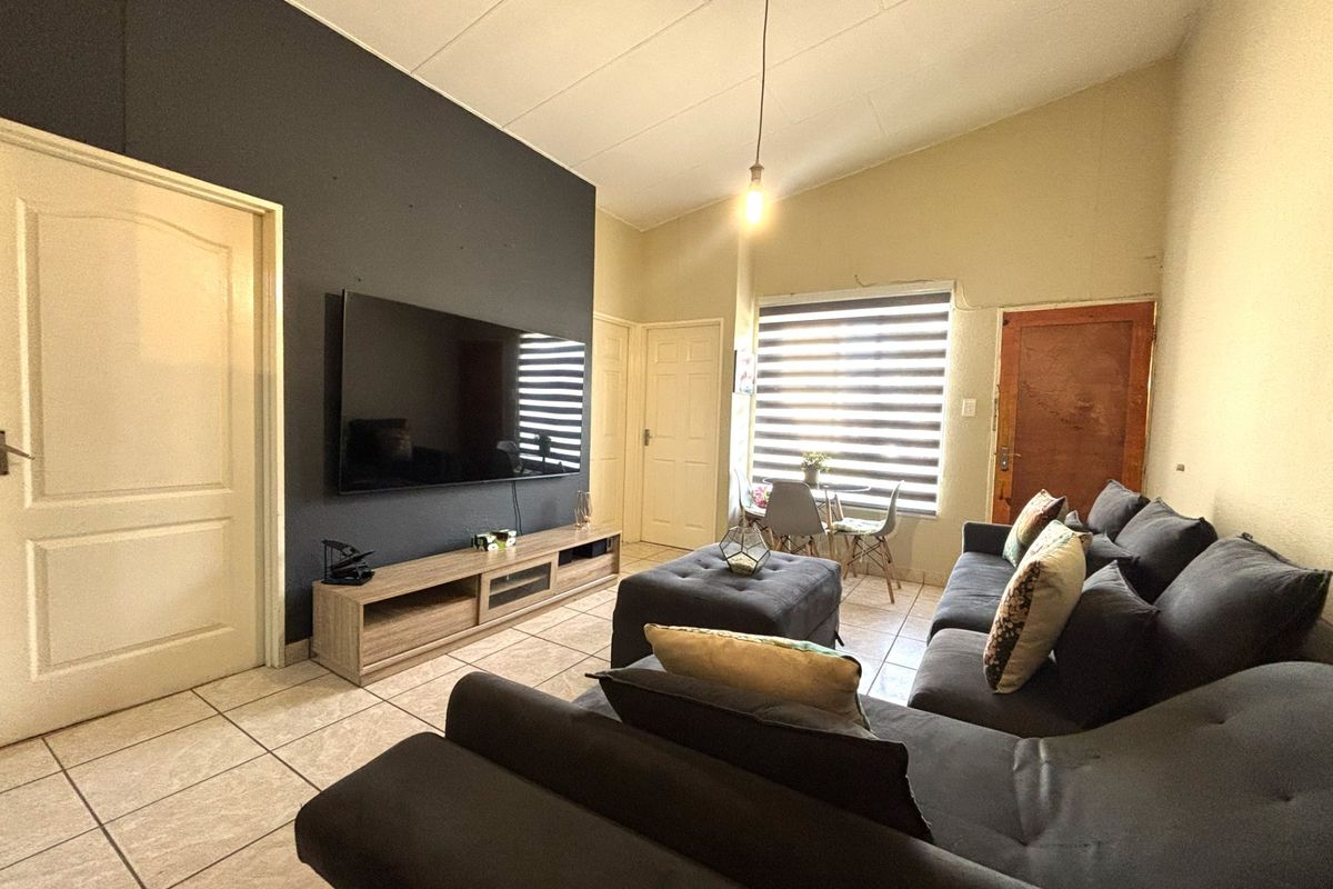 A living room featuring tiled flooring, a dark accent wall, and a vaulted ceiling with a pendant light fixture.