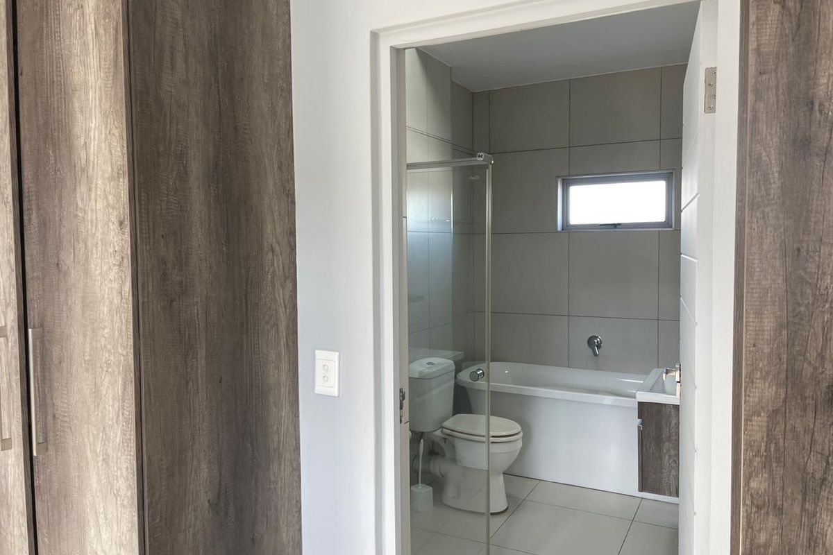 A modern bathroom featuring neutral wall tiles, a white bathtub, a toilet, and a vanity unit with integrated sink.