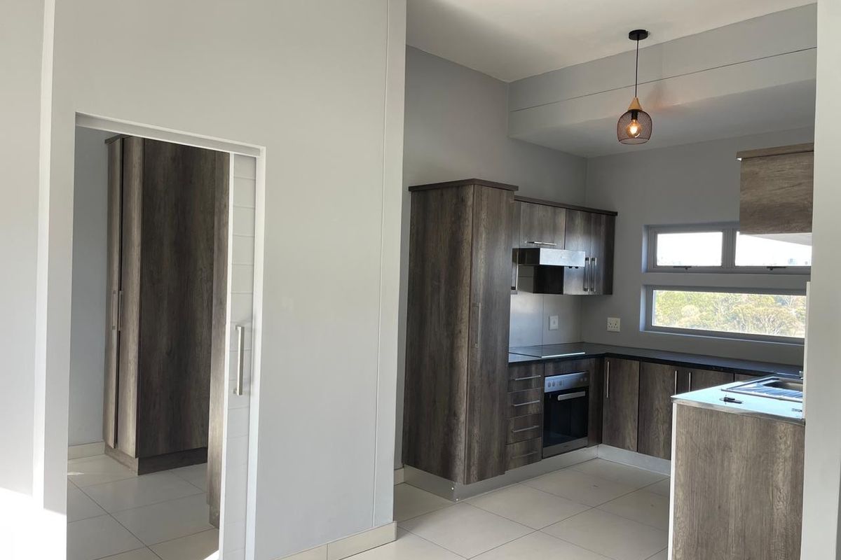 Modern kitchen featuring dark wood-grain cabinetry, built-in oven, hob, and extractor fan, with tiled flooring and a sliding door leading to an adjacent room.