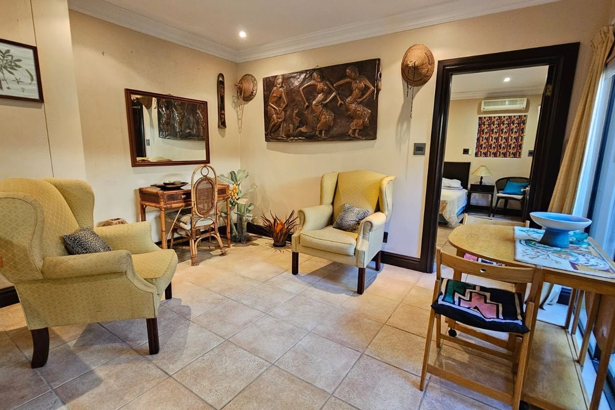 A cozy living area featuring tiled flooring, crown molding, and a seamless transition into an adjacent bedroom space.