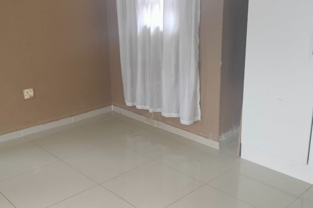 A simple, empty bedroom featuring neutral tiled flooring and a built-in white wardrobe, offering a clean canvas for personalization.