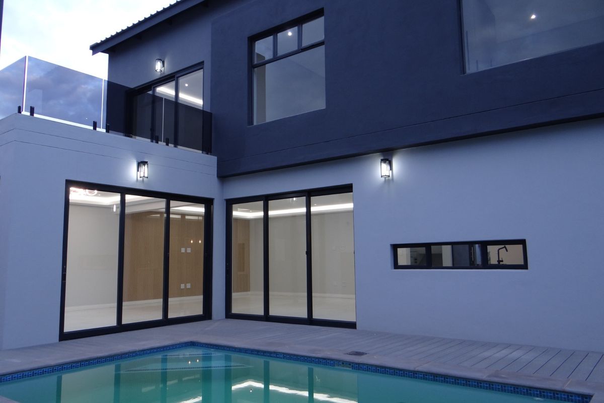 Modern two-story exterior featuring a swimming pool, glass sliding doors, balcony with glass balustrade, and contemporary dark and light facade finishes.